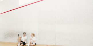 Two young squash players resting on a court, holding rackets and chatting.