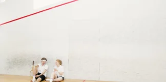 Two young squash players resting on a court, holding rackets and chatting.