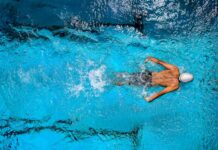 Top view of a swimmer wearing a cap, performing a front crawl stroke in a clear blue swimming pool.