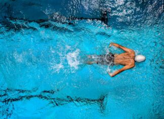 Top view of a swimmer wearing a cap, performing a front crawl stroke in a clear blue swimming pool.