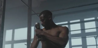 A dedicated athlete uses a massage gun to relax his muscles post-workout in the gym.