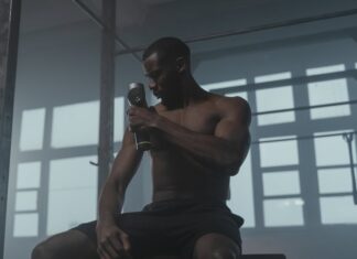 A dedicated athlete uses a massage gun to relax his muscles post-workout in the gym.
