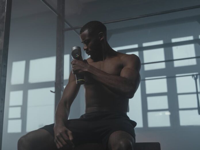 A dedicated athlete uses a massage gun to relax his muscles post-workout in the gym.