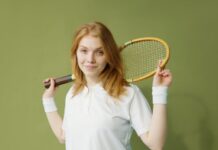 Portrait of a young caucasian woman holding a squash racket against a green background.