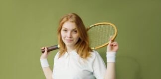 Portrait of a young caucasian woman holding a squash racket against a green background.