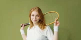 Portrait of a young caucasian woman holding a squash racket against a green background.