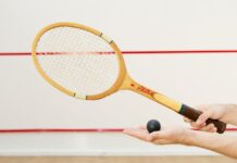 Detailed view of a squash racket and ball in hand, indoor sports scene.