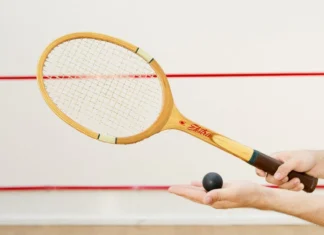Técnicas para acertar melhor a bola no squash e melhorar jogo Detailed view of a squash racket and ball in hand, indoor sports scene.
