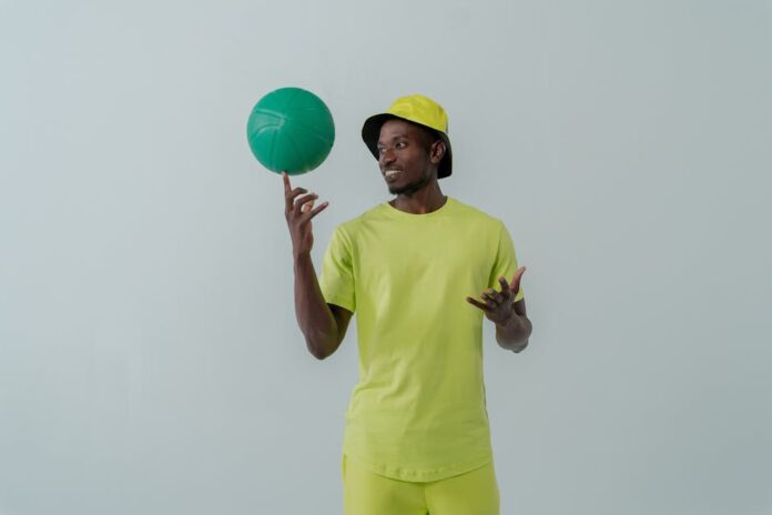 Portrait of a man in neon green clothing spinning a green ball indoors.