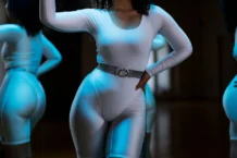 Woman in white leotard posing confidently in front of gym mirror, showcasing fitness and style.