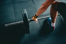Como treinar pernas no ginásio de forma eficaz e rápido Close-up of a person lifting a barbell in an indoor gym, focusing on strength training.