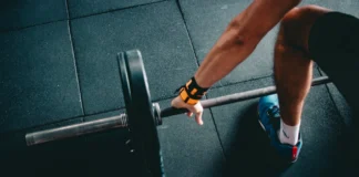 Como treinar pernas no ginásio de forma eficaz e rápido Close-up of a person lifting a barbell in an indoor gym, focusing on strength training.