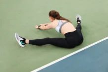 Young woman in activewear stretching on a tennis court for workout.