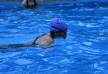 An adult female swimmer practicing in a pool, wearing goggles and swim cap.