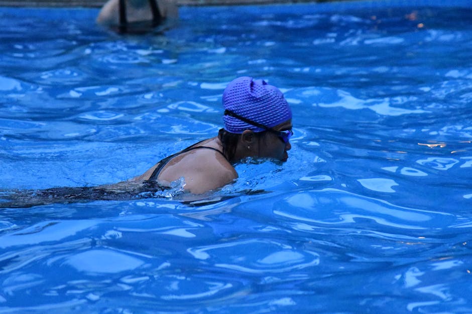An adult female swimmer practicing in a pool, wearing goggles and swim cap.