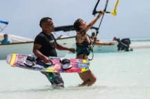 As melhores praias para iniciantes no surf Man assisting woman with kitesurfing on a sunny tropical beach, enjoying the thrill and recreation.