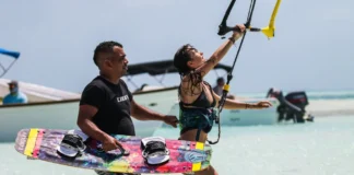 As melhores praias para iniciantes no surf Man assisting woman with kitesurfing on a sunny tropical beach, enjoying the thrill and recreation.