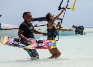 Man assisting woman with kitesurfing on a sunny tropical beach, enjoying the thrill and recreation.