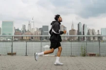 Adult man jogging along a waterfront with the New York City skyline in the background, exuding a vibrant urban lifestyle.