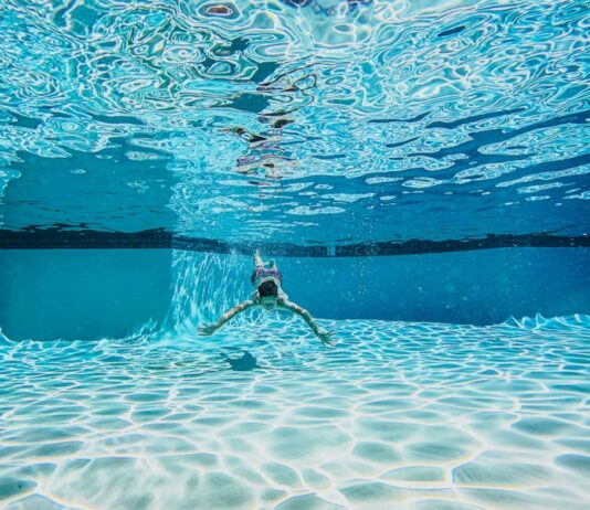 Técnicas de respiração para nadar melhor e aumentar sua performance Dynamic underwater view of a person swimming in a clear pool.