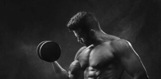 Treino de Crossfit para ganhar força: Descubra o segredo Powerful black and white portrait of a shirtless bodybuilder lifting dumbbells in the gym.