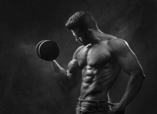 Powerful black and white portrait of a shirtless bodybuilder lifting dumbbells in the gym.