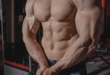 Shirtless male bodybuilder showing muscular torso and defined arms in a gym setting.