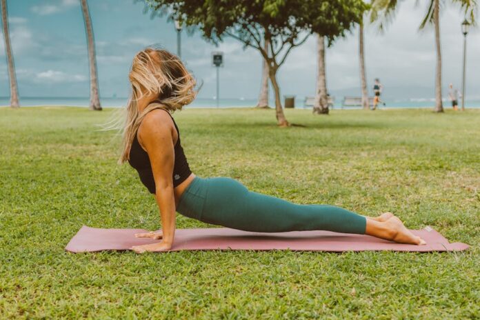 Como Manter Rotina de Treino nas Férias de Natal sem Stress! A woman practices yoga in a park, enjoying the outdoors. Perfect for wellness and fitness themes.