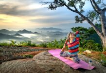 Senior woman practices yoga outdoors on a mountain at sunset, embracing wellness and serenity.