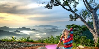 Senior woman practices yoga outdoors on a mountain at sunset, embracing wellness and serenity.