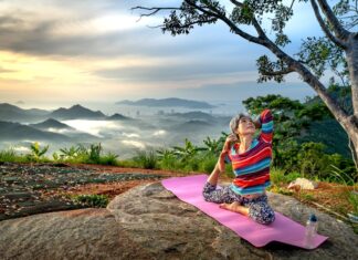 Senior woman practices yoga outdoors on a mountain at sunset, embracing wellness and serenity.