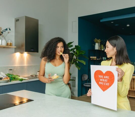 7 Hábitos saudáveis que transformam sua vida Two women discussing nutrition in a kitchen, holding health-related posters.