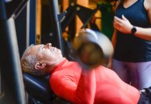 Descubra as melhores academias em Portugal para transformar-se Elderly man exercising with a barbell at the gym under supervision.