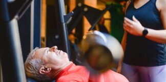 Descubra as melhores academias em Portugal para transformar-se Elderly man exercising with a barbell at the gym under supervision.