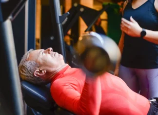 Descubra as melhores academias em Portugal para transformar-se Elderly man exercising with a barbell at the gym under supervision.