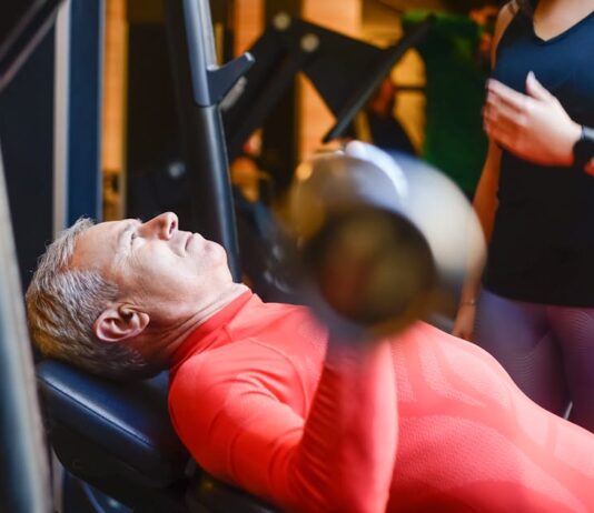 Descubra as melhores academias em Portugal para transformar-se Elderly man exercising with a barbell at the gym under supervision.
