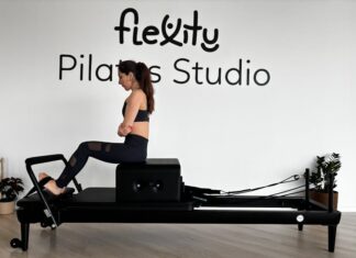 Descubra os benefícios do Pilates Clínico para a sua saúde Focused woman practicing on a Pilates reformer in a modern studio.