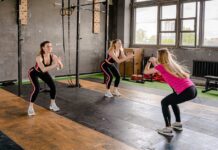 Exercícios para melhorar a postura: Descubra os segredos A group of women exercising inside a gym, performing squats in sportswear.