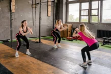 Exercícios para melhorar a postura: Descubra os segredos A group of women exercising inside a gym, performing squats in sportswear.