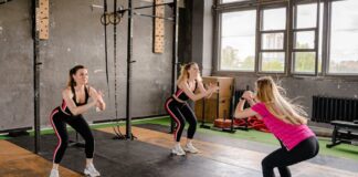 Exercícios para melhorar a postura: Descubra os segredos A group of women exercising inside a gym, performing squats in sportswear.