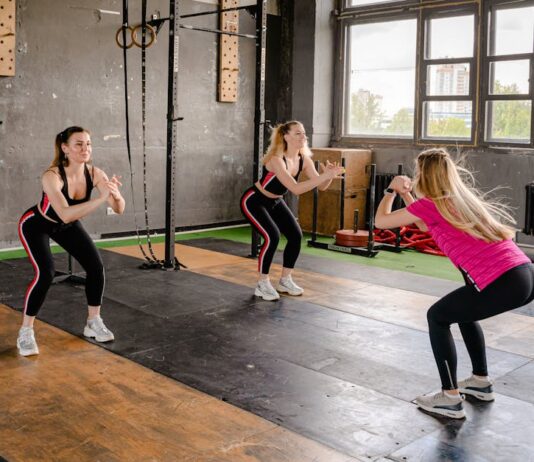 Exercícios para melhorar a postura: Descubra os segredos A group of women exercising inside a gym, performing squats in sportswear.