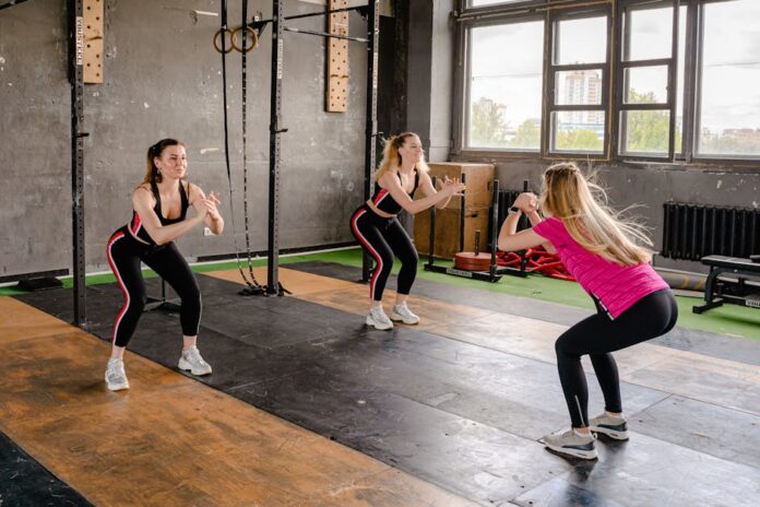 Exercícios para Melhorar a Postura: Descubra os Segredos! A group of women exercising inside a gym, performing squats in sportswear.