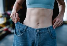 A woman shows her weight loss by holding oversized jeans revealing her toned stomach.