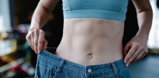 Exercícios para perder barriga em casa: Resultados em 21 dias A woman shows her weight loss by holding oversized jeans revealing her toned stomach.
