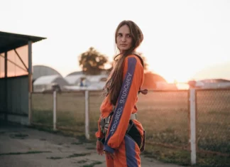 Macacão desportivo: Conforto e estilo para todas as atividades Side view of young contemplative female in skydiving jumpsuit with straps looking away on roadway against aerodrome at sunset