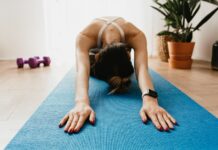 Rotina de exercícios para quem não treina: Comece hoje Woman doing a child's pose on a blue yoga mat at home, promoting fitness and wellbeing.