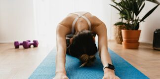 Rotina de exercícios para quem não treina: Comece hoje Woman doing a child's pose on a blue yoga mat at home, promoting fitness and wellbeing.