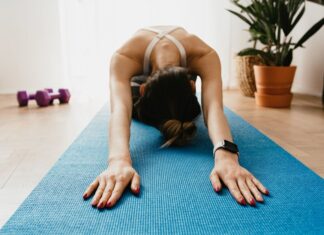 Woman doing a child's pose on a blue yoga mat at home, promoting fitness and wellbeing.