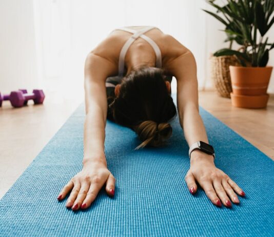 Rotina de exercícios para quem não treina: Comece hoje Woman doing a child's pose on a blue yoga mat at home, promoting fitness and wellbeing.