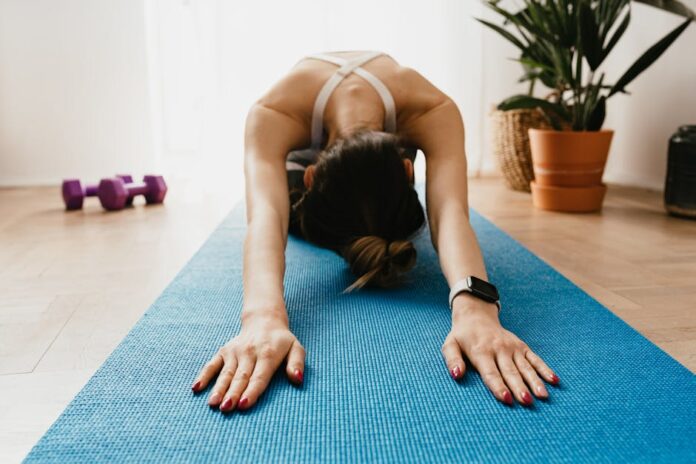 Rotina de Exercícios para Quem Não Treina: Comece Hoje! Woman doing a child's pose on a blue yoga mat at home, promoting fitness and wellbeing.